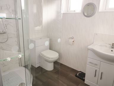A bathroom with a shower, toilet, sink, mirror, and scale at Gwersyllt in Benllech