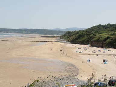 A sandy beach with people, tents, and a rocky shoreline next to green hills at Gwersyllt in Benllech