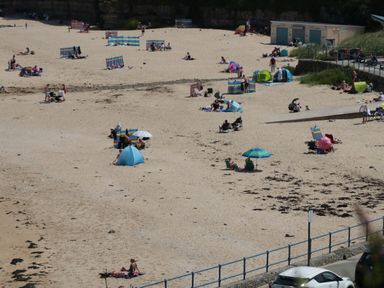 A sandy beach with people sitting under umbrellas and tents beside a road with parked cars at Gwersyllt in Benllech