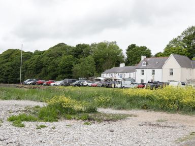 A row of parked cars in front of white buildings with greenery and yellow flowers in the foreground at Gwersyllt in Benllech