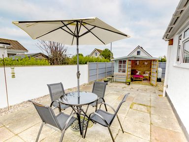 A patio with a table umbrella and four chairs and a wooden summerhouse in a backyard at Gwersyllt in Benllech