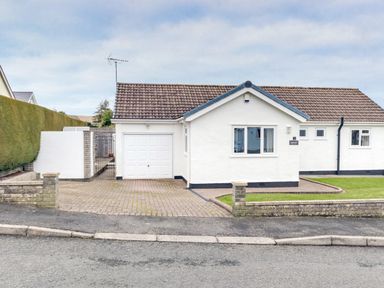 A white house with a garage a driveway and a small lawn at Gwersyllt in Benllech