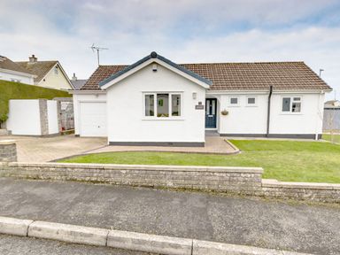 A single-story white house with a tiled roof a front lawn a paved driveway and a garage at Gwersyllt in Benllech