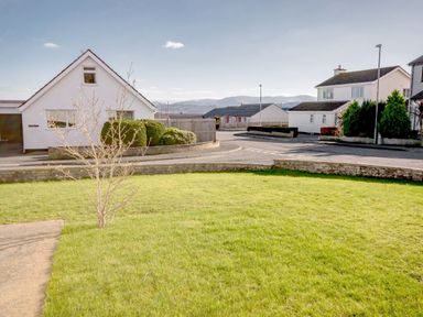 A grassy front yard with a small tree and houses in the background in Gwersyllt Benllech