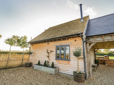 An exterior view of a wooden house with a stone wall and potted plants at The Hyde in Armscote near Newbold on Stour