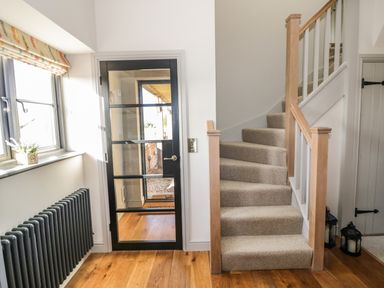 A hallway with a carpeted staircase a black frame glass door and wooden floor at The Hyde in Armscote near Newbold on Stour