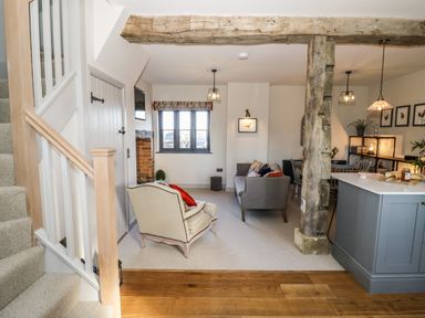 A living room with two chairs a wooden beam and staircase at The Hyde in Armscote near Newbold on Stour