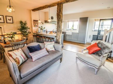 An open living room and kitchen area with a sofa and armchair and kitchen island with stools at The Hyde in Armscote near Newbold on Stour