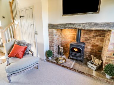 A room with a brick fireplace and a wood burning stove with a chair and cushions nearby at The Hyde in Armscote near Newbold on Stour