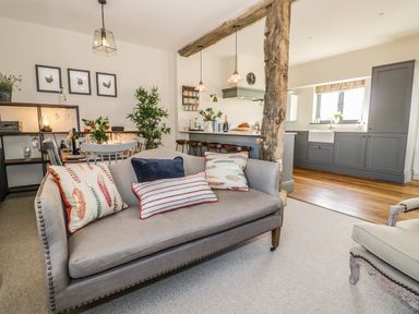 An open living room with a sofa and cushions next to a dining table and a kitchen with grey cabinets at The Hyde in Armscote near Newbold on Stour