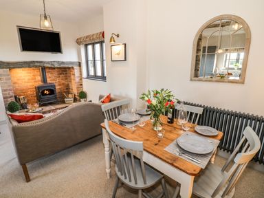 A dining area with a wooden table set for four and a living area with a sofa facing a brick fireplace with a wood stove at The Hyde in Armscote near Newbold on Stour