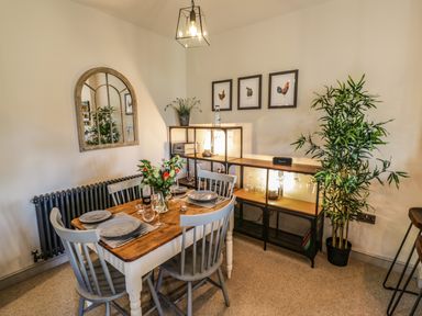 A dining room with a wooden table set for four and a shelving unit with glassware and plants at The Hyde in Armscote near Newbold on Stour