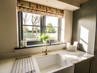 A kitchen sink under a window with soap dispensers and flowers on the windowsill at The Hyde in Armscote near Newbold on Stour