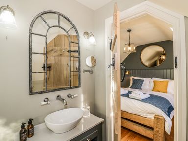 A bathroom with a sink and arched mirror next to a bedroom with a bed and round mirror at The Hyde in Armscote near Newbold on Stour