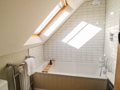 A bathroom with a bathtub under a skylight window and a towel on a rail at The Hyde in Armscote near Newbold on Stour
