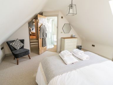 A bedroom with a bed, a chair, a dresser, and an open door leading to a bathroom at The Hyde in Armscote near Newbold on Stour