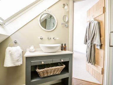 A bathroom vanity with a round mirror towels and a robe hanging on the bathroom door at The Hyde in Armscote near Newbold on Stour