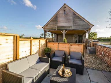 An outdoor seating area with a sofa and two chairs around a table with drinks and snacks at The Hyde in Armscote near Newbold on Stour