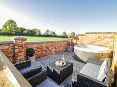 An outdoor patio with wicker seating a hot tub and a table with drinks at The Hyde in Armscote near Newbold on Stour