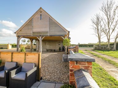An outdoor seating area with wicker chairs near a wooden building with a gravel driveway and brick walls at The Hyde in Armscote near Newbold on Stour