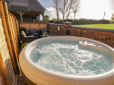 An outdoor hot tub with bubbling water next to a seating area with chairs and a table at The Hyde in Armscote near Newbold on Stour
