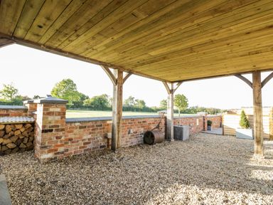 An outdoor covered area with a wooden roof brick wall and gravel ground at The Hyde in Armscote near Newbold on Stour