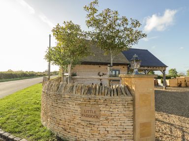 A stone wall with a sign reading little paddock trees and a wooden building behind near a road at The Hyde in Armscote near Newbold on Stour
