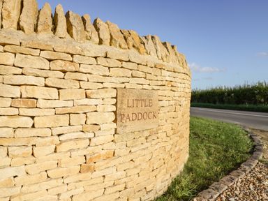A curved stone wall with a plaque reading little paddock by a roadside with grass at The Hyde in Armscote near Newbold on Stour