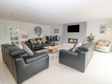 A living room with black leather sofas a coffee table a wall-mounted tv and a fireplace at Berllan in Llanbedrgoch near Benllech