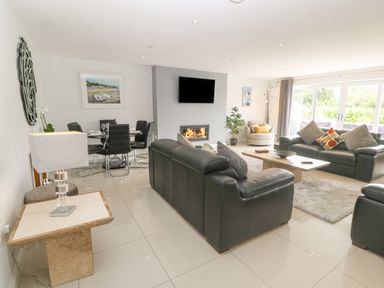 A living room with black leather sofas a fireplace a dining table with black chairs and large windows at Berllan in Llanbedrgoch near Benllech
