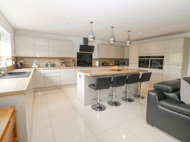 A kitchen with an island and bar stools near a black sofa at Berllan in Llanbedrgoch near Benllech