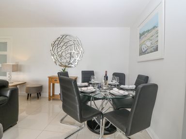A dining area with a round glass table set with plates wine glasses and a wine bottle surrounded by six black chairs at Berllan Llanbedrgoch near Benllech
