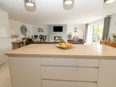 An open living area with a kitchen island in the foreground sofas a fireplace wall-mounted tv and sliding glass doors at Berllan Llanbedrgoch near Benllech