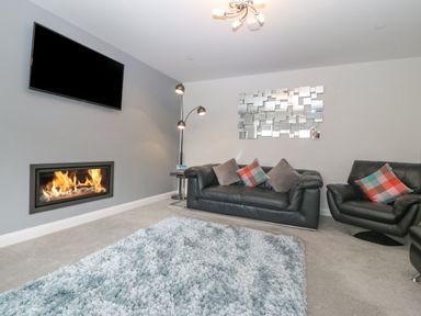 A living room with a wall-mounted TV a fireplace leather sofas a floor lamp and a textured rug at Berllan in Llanbedrgoch near Benllech
