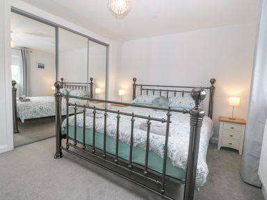 A bedroom with a metal bed frame a bed with patterned bedding two bedside tables with lamps and mirrored sliding closet doors at Berllan in Llanbedrgoch near Benllech