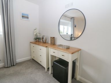 A room with a dresser and a vanity table with a circular mirror above them at Berllan in Llanbedrgoch near Benllech