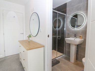 A bathroom with a shower, sink, and round mirror next to a hallway with a dresser and round wall mirror at Berllan in Llanbedrgoch near Benllech