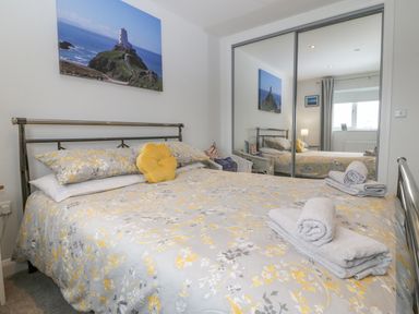 A bedroom with a bed covered in floral bedding a yellow cushion towels on the bed a mirrored wardrobe and a window at Berllan in Llanbedrgoch near Benllech