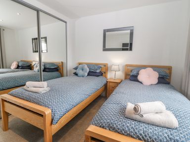 A bedroom with two single beds blue bedding flower shaped pillows a nightstand with a lamp and a mirrored wardrobe at Berllan in Llanbedrgoch near Benllech