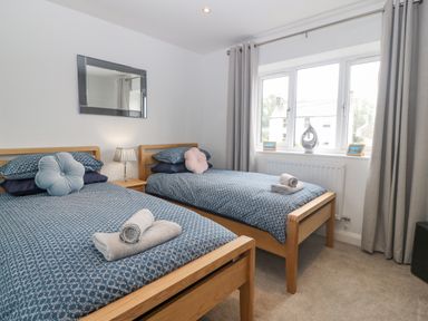 A bedroom with two single beds a bedside table with lamp a window with curtains and towels on beds at Berllan in Llanbedrgoch near Benllech