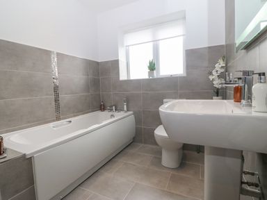 A bathroom with a bathtub a toilet and a sink with a window above at Berllan in Llanbedrgoch near Benllech