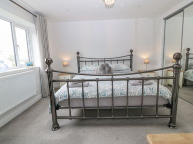 A bedroom with a metal bed frame two bedside tables with lamps a window with curtains and mirrored wardrobes at Berllan in Llanbedrgoch near Benllech