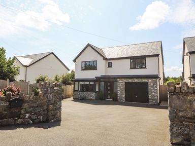 A detached house with a stone wall and driveway at Berllan in Llanbedrgoch near Benllech