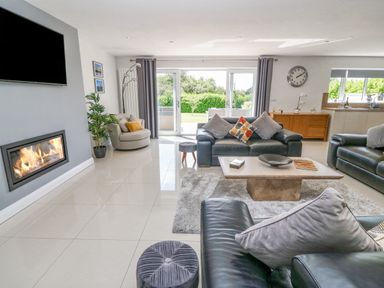 A living room with leather sofas a fireplace a coffee table and sliding glass doors at Berllan in Llanbedrgoch near Benllech
