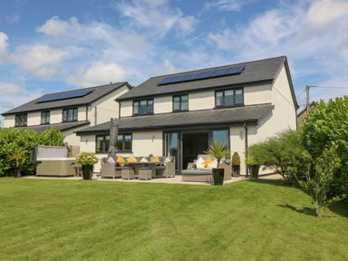 A backyard with patio furniture and a hot tub behind a modern house with solar panels at Berllan in Llanbedrgoch near Benllech