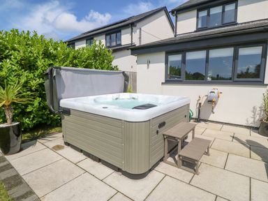 An outdoor patio area with a hot tub with steps next to a house with windows at Berllan in Llanbedrgoch near Benllech