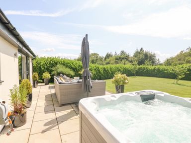 An outdoor patio with a hot tub seating area umbrellas and plants overlooking a grassy garden at Berllan in Llanbedrgoch near Benllech