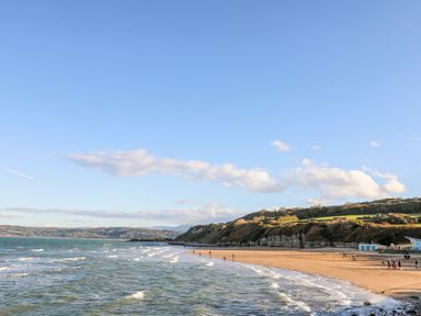 A beach with people walking along the shore and hills in the background at Berllan in Llanbedrgoch near Benllech