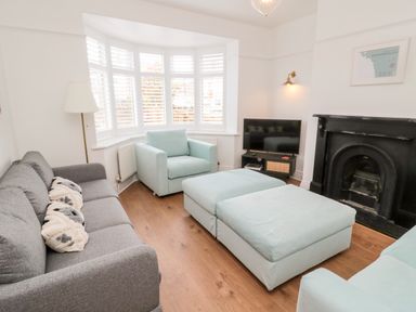 A living room with a gray sofa light blue chairs two ottomans a black fireplace a TV and a floor lamp at Shileen in Seahouses