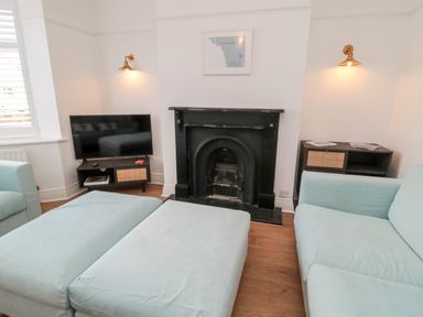 A living room with a light blue sofa and ottoman a black fireplace a television on a stand and wall lights at Shileen in Seahouses